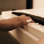 A close-up view of a hand with painted nails gently playing piano keys, creating a serene musical moment.