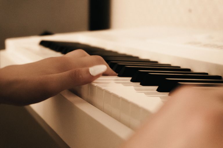 A close-up view of a hand with painted nails gently playing piano keys, creating a serene musical moment.